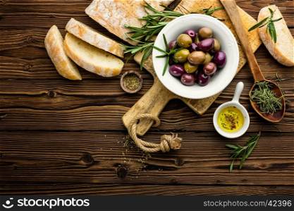 italian food ingredients, rosemary, olives, olive oil and ciabatta bread on wooden background