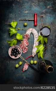 Italian food lifestyle with salami, red wine, grape leaves and olives on dark background, top view. Flat lay of italian food