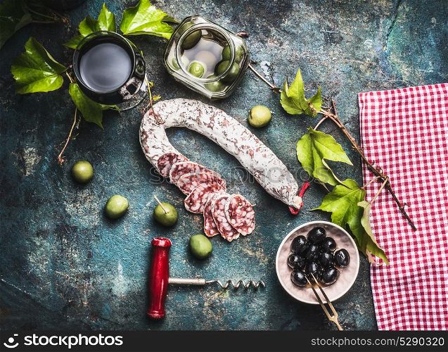 Italian food still life with glass of red wine, olives and sausage on rustic background, top view