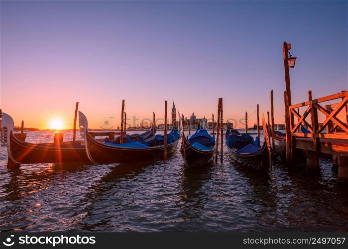 Italian gondolas moored to the poles in Europe Venice near the city center and Saint Mark square with a background view of the church of San Giorgio Maggiore at sunrise