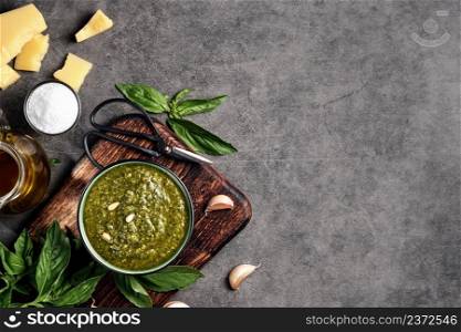 Italian green basil pesto in a gravy boat garnished with pine nuts. Ingredients for making pesto. Layout on gray kitchen table with copy space