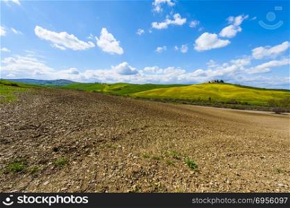Italian landscape with meadows early in the spring. Agriculture in Italy, plowed fields, pastures and farmhouse on the hill.. Plowed fields, pastures and farmhouse