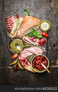 Italian meat plate with various antipasti, ciabatta bread, pesto and ham on rustic wooden background, top view. Italian food and snack concept.