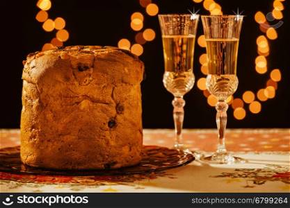 Italian panettone and sparkling wine over a table with Christmas lights on background. Italian panettone and sparkling wine over a table