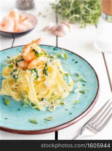 Italian pasta fettuccine in a creamy sauce with shrimp and spinach on a plate, high angle view