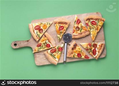 Italian pizza slices on wooden cutting board and green background. Above view of pizza primavera slices. Tasty spring food. Traditional italian meal.