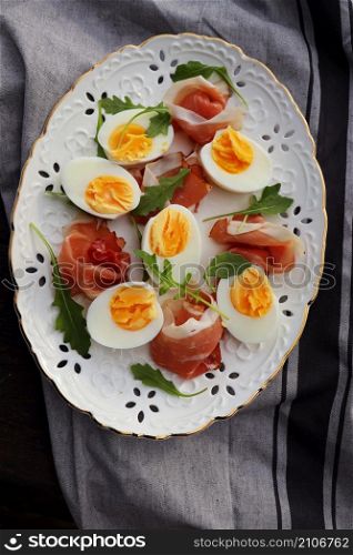 Italian salad. Boiled eggs with smoked ham and arugula on white plate. Dark wooden background