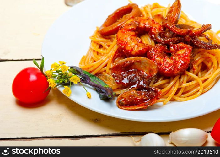 Italian seafood spaghetti pasta on red tomato sauce over white rustic wood table