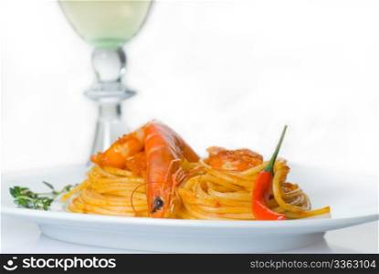 italian spaghetti pasta and fresh spicy shrimps sauce,with a grass of dry white wine on background