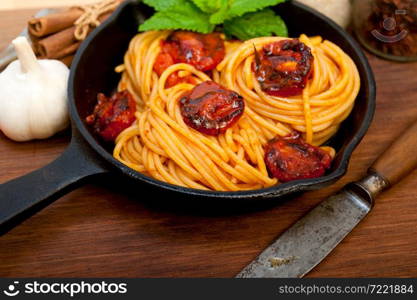 italian spaghetti pasta and tomato with mint leaves on iron skillet over wood board