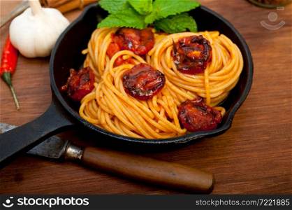 italian spaghetti pasta and tomato with mint leaves on iron skillet over wood board