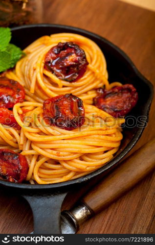 italian spaghetti pasta and tomato with mint leaves on iron skillet over wood board