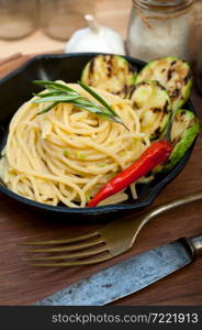 italian spaghetti pasta with zucchini sauce on iron skillet over wood board