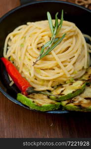 italian spaghetti pasta with zucchini sauce on iron skillet over wood board