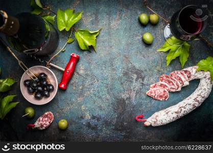 Italian still life with salami, red wine, olives and grape leaves on dark rustic background, top view, place for text. Italian food background