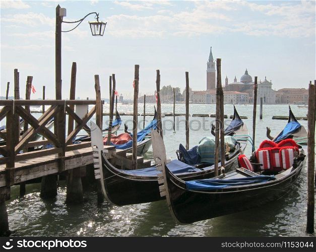 Italian traditional boats - gondolas parking near old wooden pier on the background of view of San Giorgio Maggior Church, Venice, Italy.. Traditional italian gondolas parking near berth.