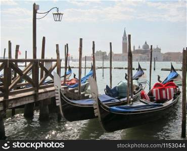Italian traditional boats - gondolas parking near old wooden pier on the background of view of San Giorgio Maggior Church, Venice, Italy.. Traditional italian gondolas parking near berth.