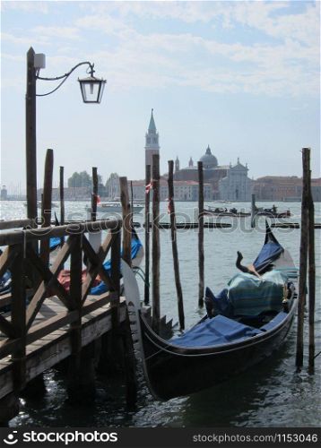Italian traditional gondola parking near old wooden berth on the background of view of San Giorgio Maggior Church Venice, Italy.. Old wooden pier with parking italian tradition gondola.