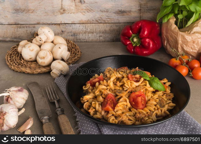 Italian wholemeal pasta with tuna, mushrooms and basil. Fresh pasta with tuna and tomato sauce on old wooden background. Italian cuisine concept.