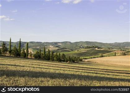 Italian wine farm surrounded with plowed sloping hills of Tuscany in the autumn. Rural landscape with vineyard, olive trees and fields after harvest.