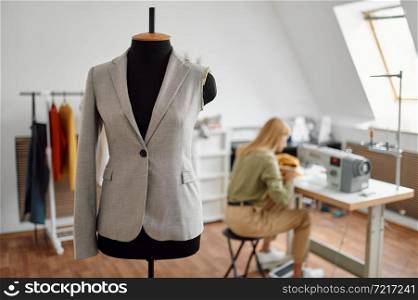 Jacket on mannequin, dressmaker at the sewing machine on background. Dressmaking occupation, handmade tailoring business, handicraft hobby. Jacket on mannequin, dressmaker at sewing machine