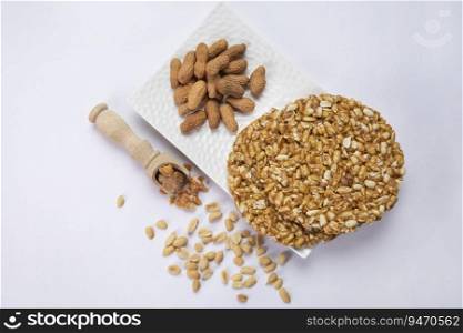 Jaggery in a wooden spoon with plain peanuts kept with chikki and groundnuts on a white tray