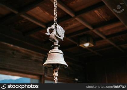 Japanese Buddhist temple or shinto shrine antique bronze bell hanging on metal chain under wooden ceiling.