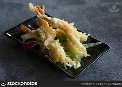 Japanese Cuisine - Tempura Shrimps (Deep Fried Shrimps) with sauce and vegetables on a black plate. Gray background,shallow depth of field