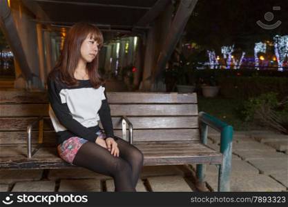 Japanese female looking sad sitting on a brown park bench