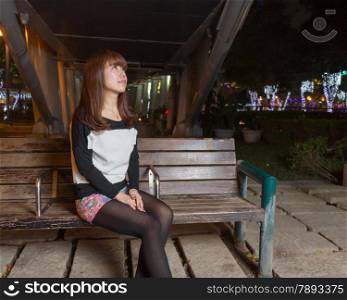 Japanese female looking sad sitting on a brown park bench