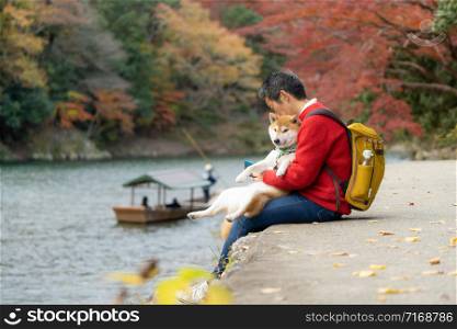 Japanese man and his buddy Chiba dog sit resting along the arashiyama river on a holiday to see the atmosphere of autumn leaves in Tokyo.