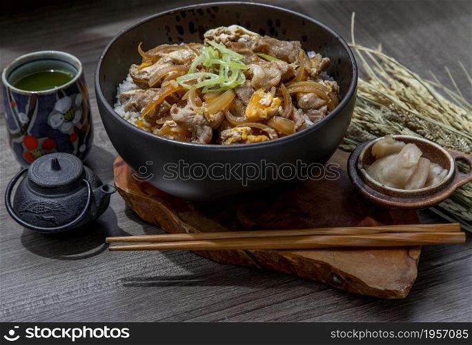 Japanese pork rice bowl with egg and onion (Donburi) served with pickled ginger and green tea on wooden table. Japanese food style.