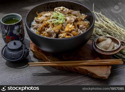 Japanese pork rice bowl with egg and onion (Donburi) served with pickled ginger and green tea on wooden table. Japanese food style.