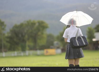 Japanese school with umbrella on rain in countryside with grass mountain and tree