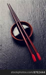 Japanese sushi chopsticks over soy sauce bowl on black stone background