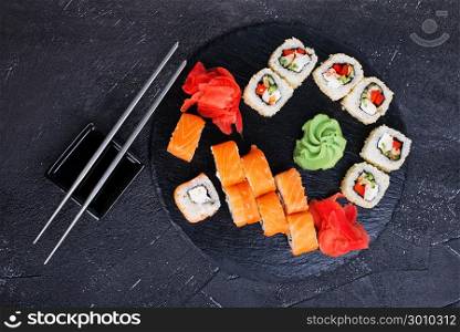 Japanese sushi on a rustic dark background. Sushi rolls and ginger, wasabi, soy sauce.
