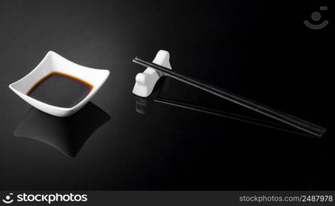 japanese sushi sticks and sauce pot with soy on a black background. metal chopsticks and sauce on a dark background. sushi sticks and sauce