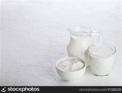 Jar and glass of milk and bowl of sour cream on white stone kitchen table background.