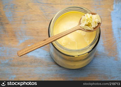 jar and spoon of ghee (clarified butter) on grunge wood - top view