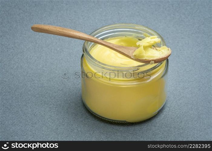 jar and spoon of ghee (clarified butter) on textured paper background