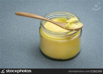 jar and spoon of ghee (clarified butter) on textured paper background