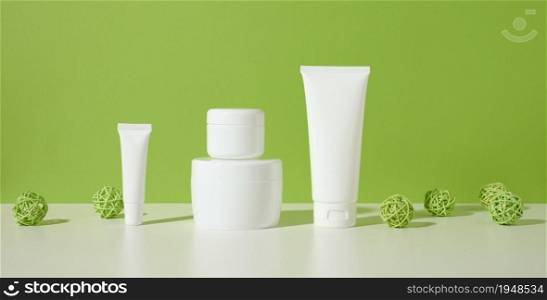 jar, empty white plastic tubes for cosmetics on a white table, green background. Packaging for cream, gel, serum, advertising and product promotion. Mock up