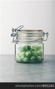 Jar filled with green mint candies on table. Plain background