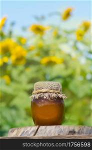 Jar of honey and sunflowers on wooden table over bokeh garden background. Empty place for text. Healthy eating concept