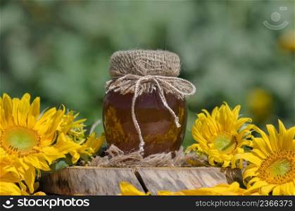 Jar of honey and sunflowers on wooden table over bokeh garden background. Jar of fresh honey in field of wildflowers. Jar of honey on wooden table