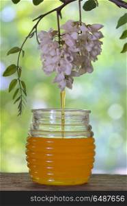 Jar of Pouring honey with flowers of acacia on table. Jar of honey with flowers of acacia on table