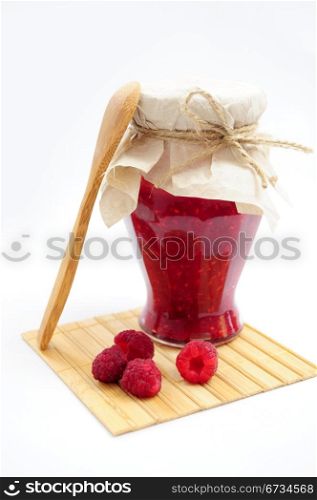Jar of raspberry jam with fresh fruits with wooden spoon on wooden coaster