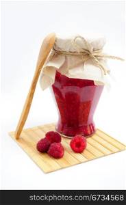 Jar of raspberry jam with fresh fruits with wooden spoon on wooden coaster