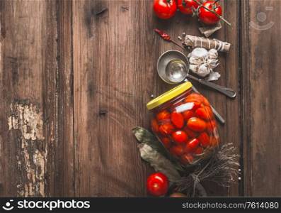 Jar with canned tomatoes on rustic kitchen table with garlic and seasonings. Preservation and conservation of crops. Healthy fermented pickled food.