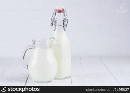 Jar with milk and vintage bottle of milk on white wooden table background